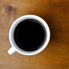 Coffee cup on wooden kitchen table. Top view with morning sunlight