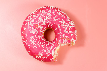 Bitten tasty pink donut on pink background. Top view
