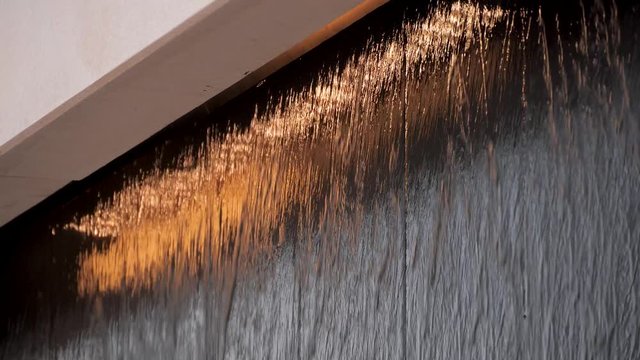 Water flows along black stone wall with orange backlight. Modern swimming pool or fountain in a shopping center. Selective focus.