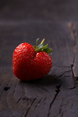 a ripe strawberry in the shape of a heart laid on a dark wooden background