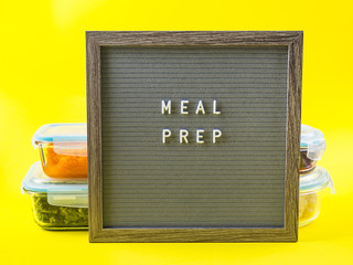 Stack of airtight glass food containers with colorful cooked vegetables on bright yellow background with letter board with text Meal Prep