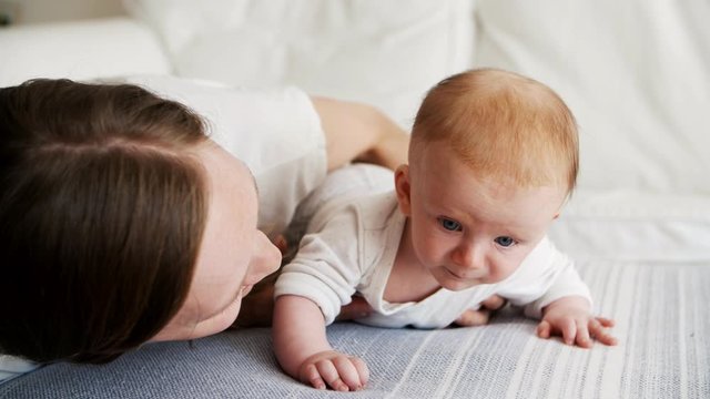 Happy mom posing with cute baby daughter, speaking and smiling. New mother nursing six month child at home. Baby care and parenthood concept