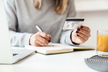 Cropped photo of woman making notes in planner while holding credit card
