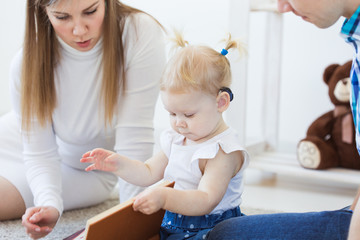 Hearing aid in baby girl's ear. Toddler child wearing a hearing aid at home. Disabled child,...