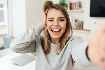 Photo of cheerful woman laughing and winking while taking selfie photo