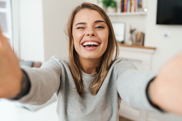 Photo of cheerful woman laughing and winking while taking selfie photo