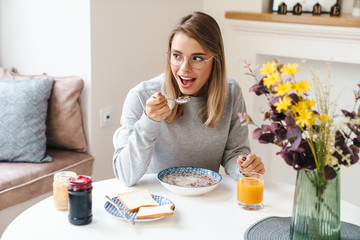 Obraz na płótnie Canvas Photo of cheerful young woman eating cereal while having breakfast