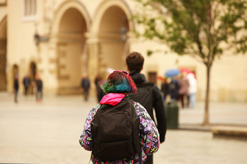 Fototapeta premium A young girl with multi-colored hair and a trendy haircut walks around the city with a backpack. Teenage protest and the war of generations. Challenge to society. Originality of behavior. Challenging