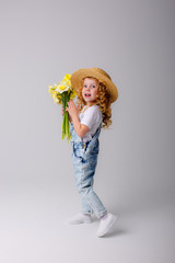 a little blonde girl with a straw hat and a bunch of spring flowers in her hands on a white background