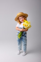 a cute little girl in a straw hat holds a bouquet of spring yellow daffodil flowers on a white background