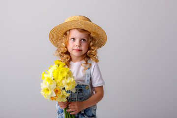 a cute little girl in a straw hat holds a bouquet of spring yellow daffodil flowers on a white background