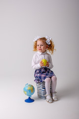 a little school girl with an Apple in her hands is sitting on books on a white background