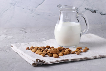 Fresh almond milk in transparent jug and almonds on gray concrete background, Healthy vegan milk replacer, Space for text, Closeup