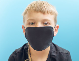 a blond boy in a protective black fabric face mask, the concept of quarantine during the coronavirus pandemic