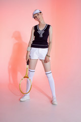Girl tennis player with a racket in sportswear and white sneakers on a pink background in the Studio with shadow.