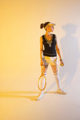 Girl tennis player with a racket in sportswear and white sneakers on a yellow background in the Studio