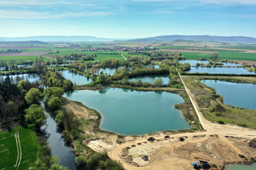 Fototapeta na wymiar Aerial view of an active gravel pond beside the river Leine near Sarstedt, Germany, with a truck and piles of sand and a village in the background