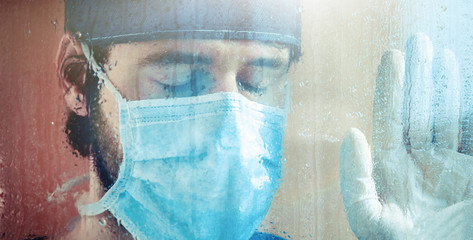 Medico o infermiere stanco guarda fuori dalla finestra dell'ospedale, bagnata dalla pioggia.