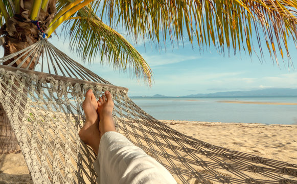 View on female feet, swinging and relaxing in hammock on a sand beach of Thailand