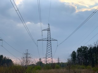 High voltage electric tower against a cloudy sky. High steel power pole, among the forest.