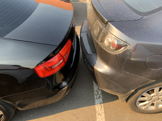 Two cars next to each other. Cars are parked very close. Small clearance from bumper to bumper.