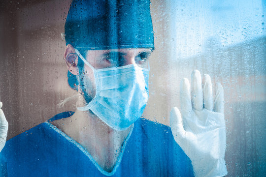 Medico o infermiere stanco guarda fuori dalla finestra dell'ospedale, bagnata dalla pioggia.