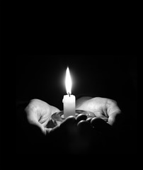 Hands holding a burning candle in dark room