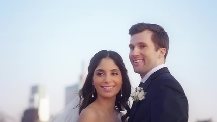 A bride's veil falls as she smiles and holds her smiling groom as they pose for pictures at their city wedding