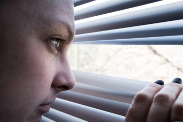 A man looks out the window opening the blinds