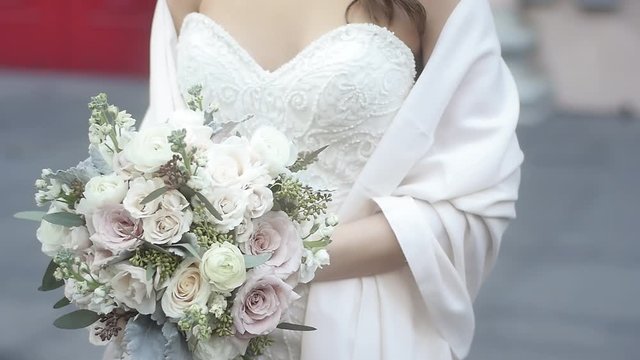 A bride with a strapless dress and a shawl holding a bouquet of light colored roses