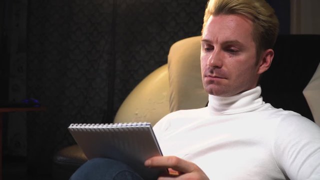 European man writes his thoughts with a pen in a notebook, serious in white clothes, straight look, medium plan