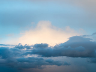 dark clouds in front of white sunlit cloud in blue sky at spring dusk