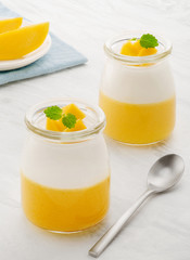 Sweet dessert of yogurt and mango with mint. Two jars with dessert on a light table