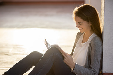 Happy teenager reading a book sitting outdoors