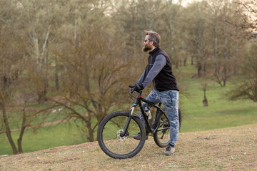 Obraz premium Sports brutal bearded guy on a modern mountain bike. Cyclist on the green hills in the spring.