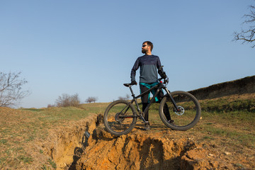 Fototapeta na wymiar Cyclist in shorts and jersey on a modern carbon hardtail bike with an air suspension fork standing on a cliff against the background of fresh green spring forest