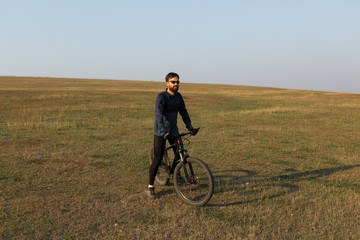 Fototapeta premium Cyclist in shorts and jersey on a modern carbon hardtail bike with an air suspension fork standing on a cliff against the background of fresh green spring forest