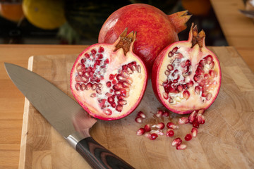 Close up of one whole and two half pomegranates fruits and a damascus kitchen knife on a wooden...