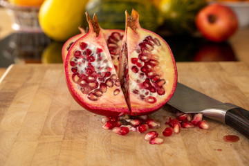 Close up of two half pomegranates fruits and a damascus kitchen knife on a wooden cutting board...