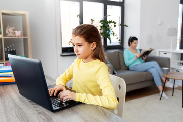 children, education and distant learning concept - student girl with laptop computer and mother reading book at home