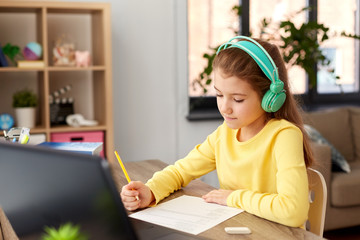 children, education and distant learning concept - student girl in headphones doing school test at...