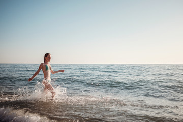 Girl in a bikini runs along the waves on the beach in summer