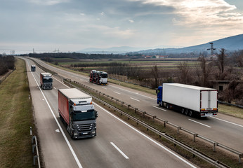 Highway transportation with a convoy of Lorry trucks passing trucks and and car transporter under a beautiful 

sunset sky