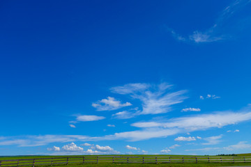 hill with green grass and a fence. light clouds on a background of blue sky. summer sunny day.