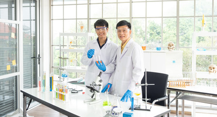 Science, Chemistry, Technology, Biology and Laboratory concept - Portrait of Asian senior and junior scientists is showing their experimental results in a test glass beaker.