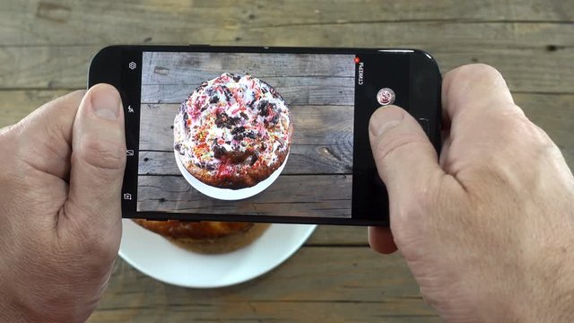 Male hands with smartphone take pictures of Easter cake in 4K. Easter holiday baking on a wooden table