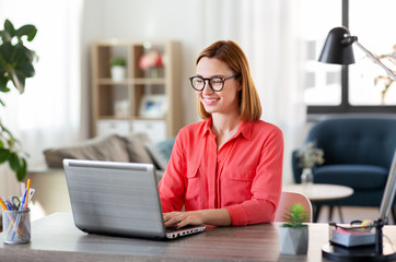 remote job, technology and people concept - happy smiling young woman in glasses with laptop...