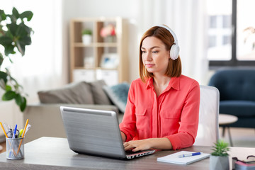 remote job, technology and people concept - young woman in headphones with laptop computer working at home office