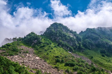 Green mountain slope with rocks on cloudy day.