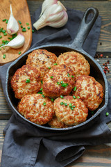 Juicy delicious chicken or Turkey cutlets with garlic and green onions in a cast iron pan on a dark wooden table. Rustic style. Selective focus, top view
